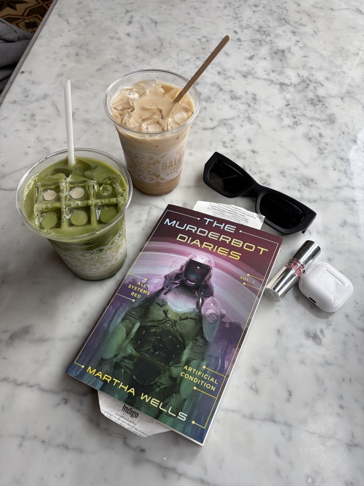 Iced drinks and The Murderbot Diaries on a cafe table